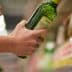 A person holding a green bottle of olive oil while reaching for another on a shelf. - Olive Oil Times