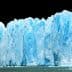 A large glacier with blue ice formations and a jagged edge against a dark background. - Olive Oil Times