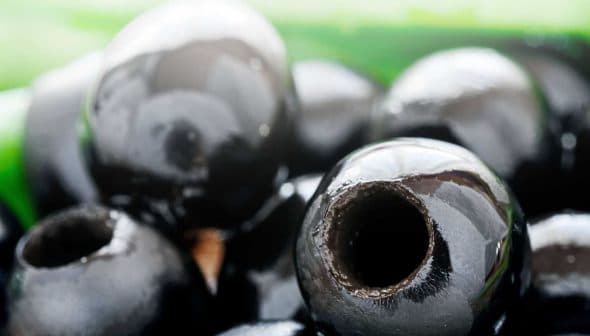 Close-up view of shiny black olives with visible holes and smooth surfaces. - Olive Oil Times