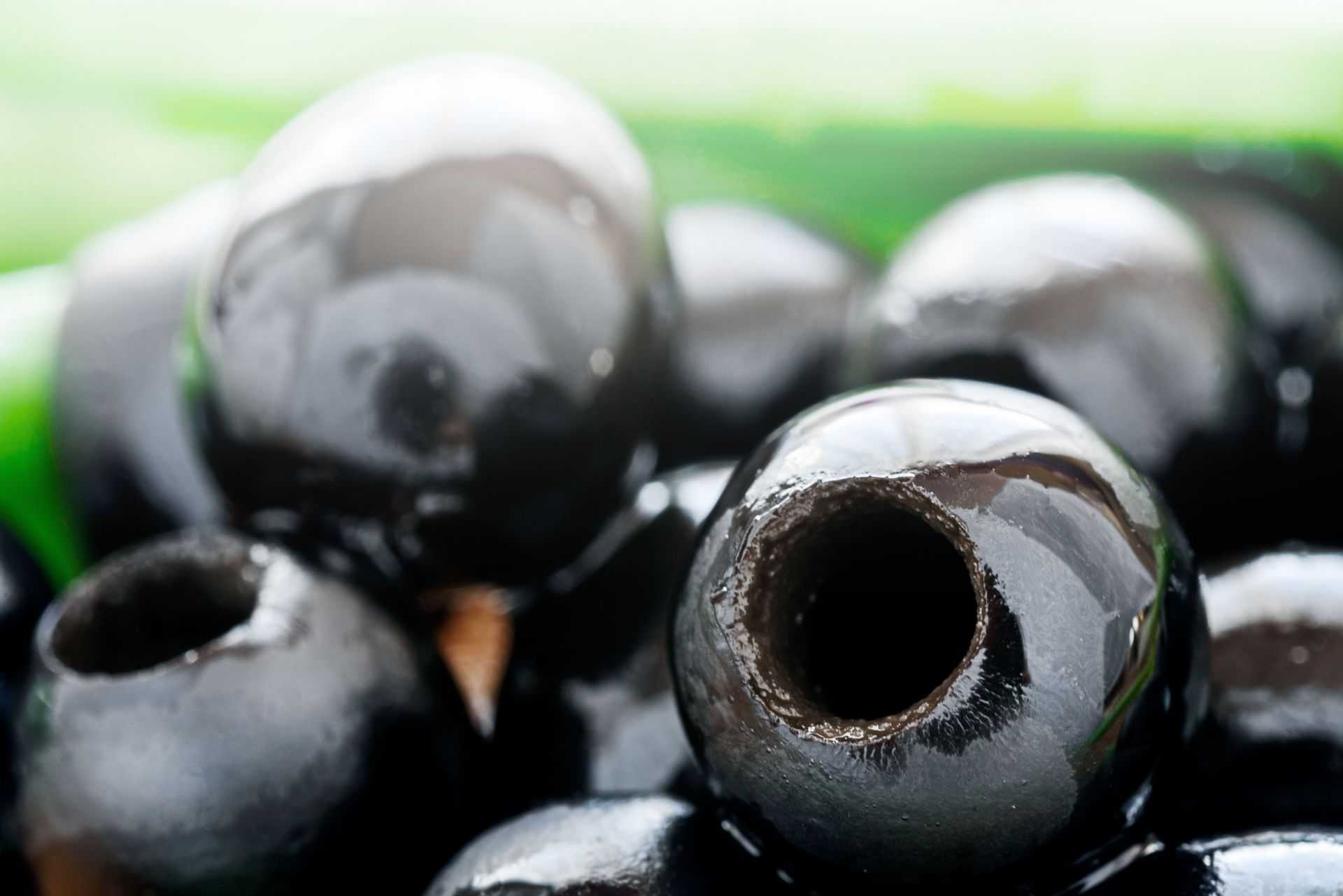 Close-up view of shiny black olives with visible holes and smooth surfaces. - Olive Oil Times