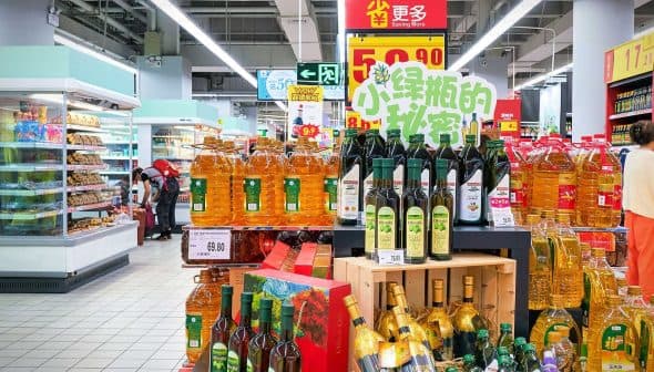 Shelves filled with different brands of cooking oils in a supermarket aisle. - Olive Oil Times