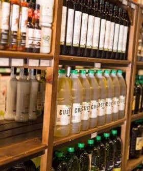 Shelves displaying various bottles of oils and condiments in a store setting. - Olive Oil Times