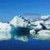 Icebergs of various shapes and sizes floating in calm water under a clear blue sky. - Olive Oil Times