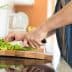 A person using a knife to chop green vegetables on a wooden cutting board in a kitchen. - Olive Oil Times