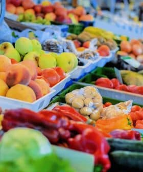 A selection of fresh fruits and vegetables displayed at a market stall, including peaches, carrots, and cucumbers. - Olive Oil Times