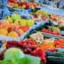 A selection of fresh fruits and vegetables displayed at a market stall, including peaches, carrots, and cucumbers. - Olive Oil Times