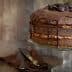Chocolate layer cake topped with chocolate ganache and chocolate chips on a glass cake stand. - Olive Oil Times