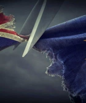 Scissors cutting through a torn British flag and a European Union flag. - Olive Oil Times