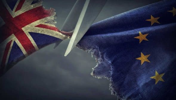 Scissors cutting through a torn British flag and a European Union flag. - Olive Oil Times