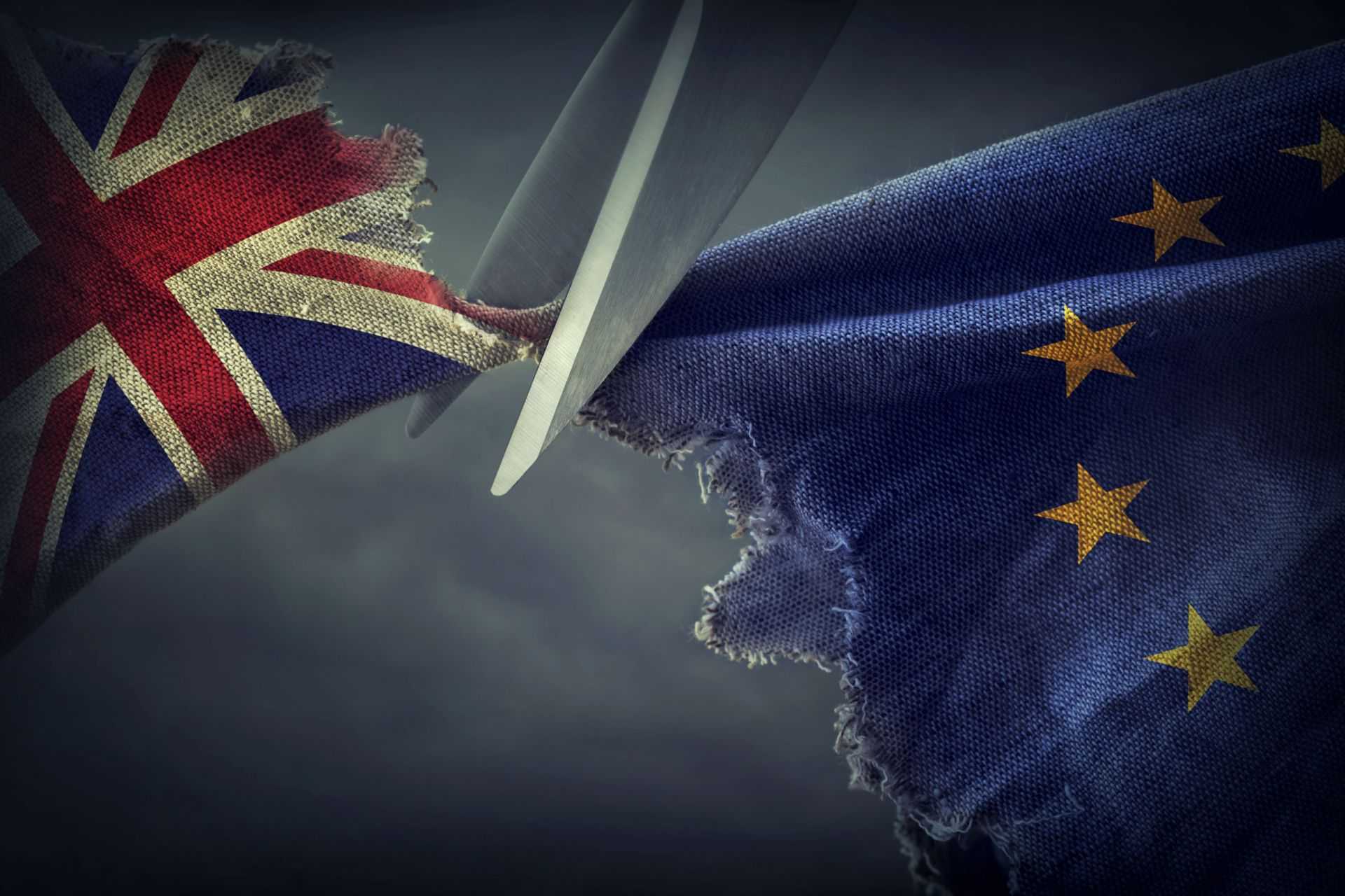 Scissors cutting through a torn British flag and a European Union flag. - Olive Oil Times