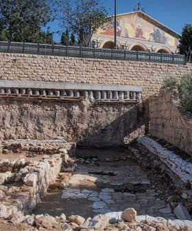 Excavation site featuring stone structures and a building in the background. - Olive Oil Times
