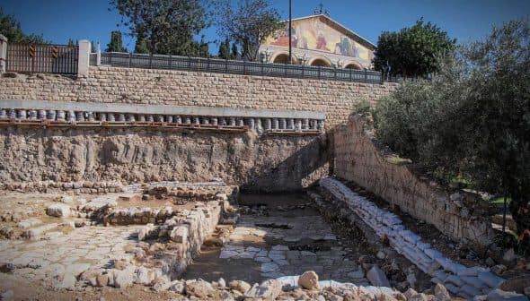 Excavation site featuring stone structures and a building in the background. - Olive Oil Times