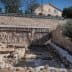 Excavation site featuring stone structures and a building in the background. - Olive Oil Times