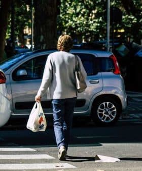 Individual walking on a street while carrying a grocery bag in one hand. - Olive Oil Times