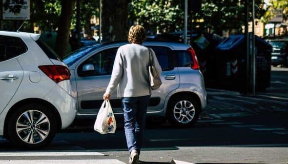 Individual walking on a street while carrying a grocery bag in one hand. - Olive Oil Times