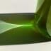 Green glass bottle casting a light reflection on a white surface. - Olive Oil Times