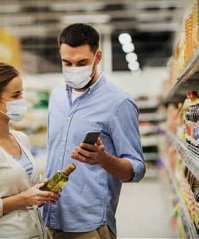 A man and woman wearing masks while shopping in a grocery store aisle, examining products. - Olive Oil Times