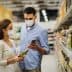 A man and woman wearing masks while shopping in a grocery store aisle, examining products. - Olive Oil Times