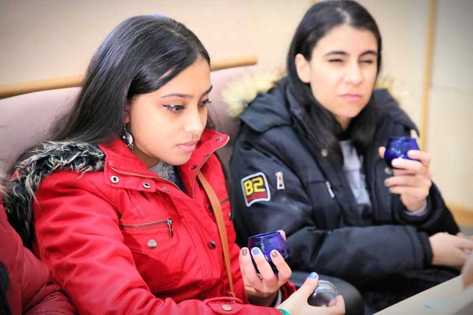 Two young women seated, one in a red jacket and the other in a black jacket, each holding a blue cup. - Olive Oil Times