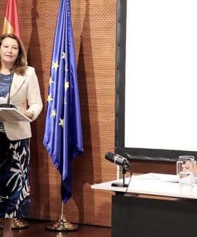 A woman presenting at a podium with flags of Spain and the European Union in the background. - Olive Oil Times