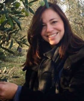 Woman smiling while picking olives from an olive tree in an outdoor setting. - Olive Oil Times