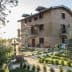 Two-story stone house with balconies and a garden featuring trees and shrubs. - Olive Oil Times