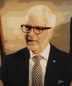 A man with white hair and glasses speaking, wearing a dark suit and patterned tie. - Olive Oil Times