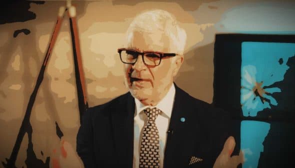 A man with white hair and glasses speaking, wearing a dark suit and patterned tie. - Olive Oil Times