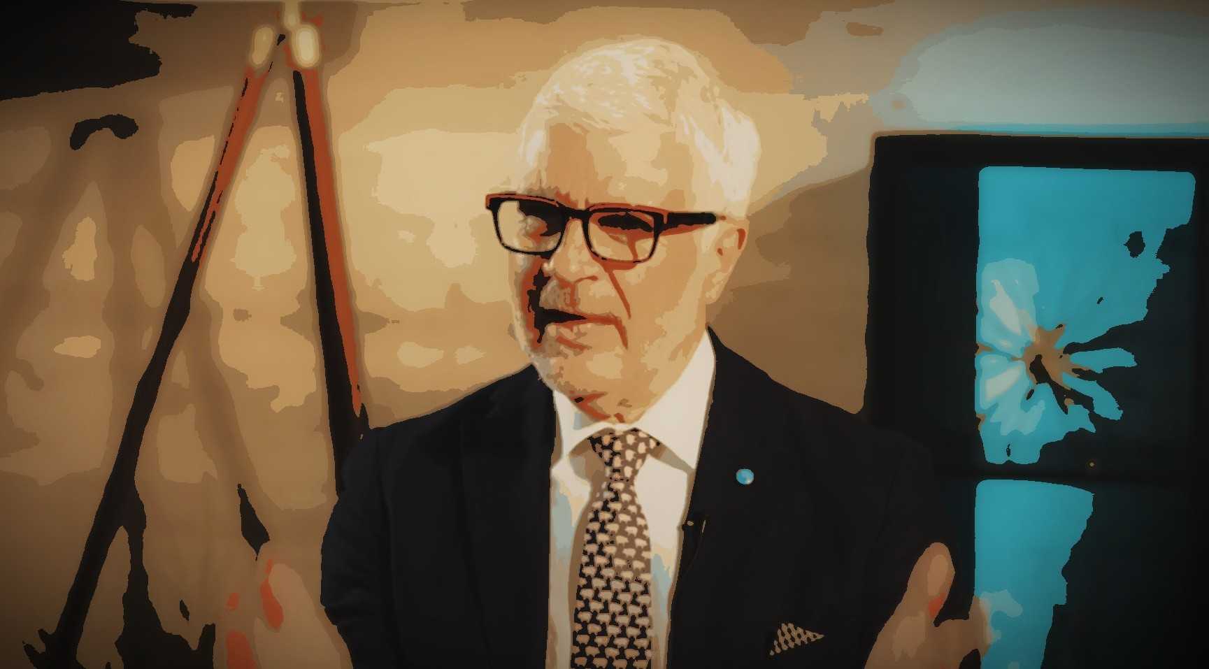 A man with white hair and glasses speaking, wearing a dark suit and patterned tie. - Olive Oil Times