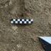 Checkerboard scale and measuring tool placed on the ground in a dirt area. - Olive Oil Times