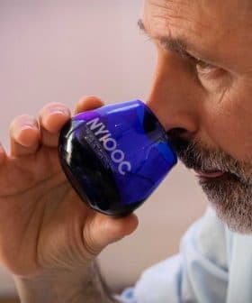 Man with a beard holding a blue glass for tasting olive oil, bringing it close to his nose. - Olive Oil Times