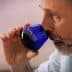 Man with a beard holding a blue glass for tasting olive oil, bringing it close to his nose. - Olive Oil Times