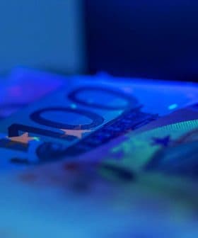 Close-up view of 100 euro banknotes with a blue hue and visible security features. - Olive Oil Times