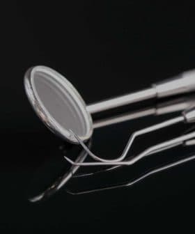 Set of dental examination instruments including a mirror and explorer on a reflective surface. - Olive Oil Times