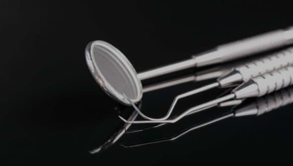 Set of dental examination instruments including a mirror and explorer on a reflective surface. - Olive Oil Times