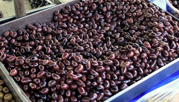 A large tray filled with dark black olives, showcasing their smooth surface and oval shape. - Olive Oil Times