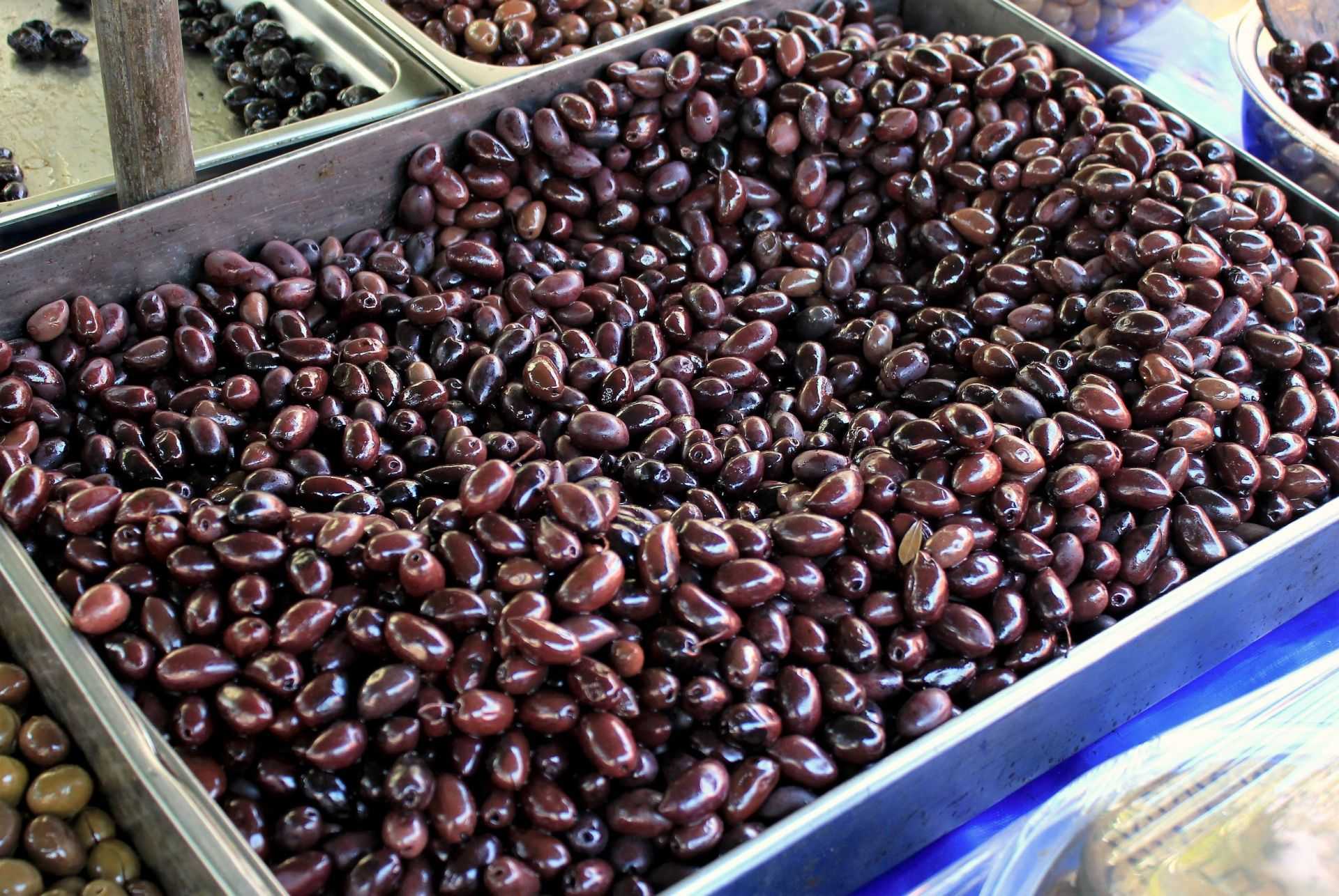 A large tray filled with dark black olives, showcasing their smooth surface and oval shape. - Olive Oil Times