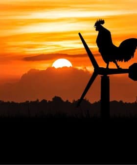 Silhouette of a rooster standing on a wind turbine with a sunset in the background. - Olive Oil Times