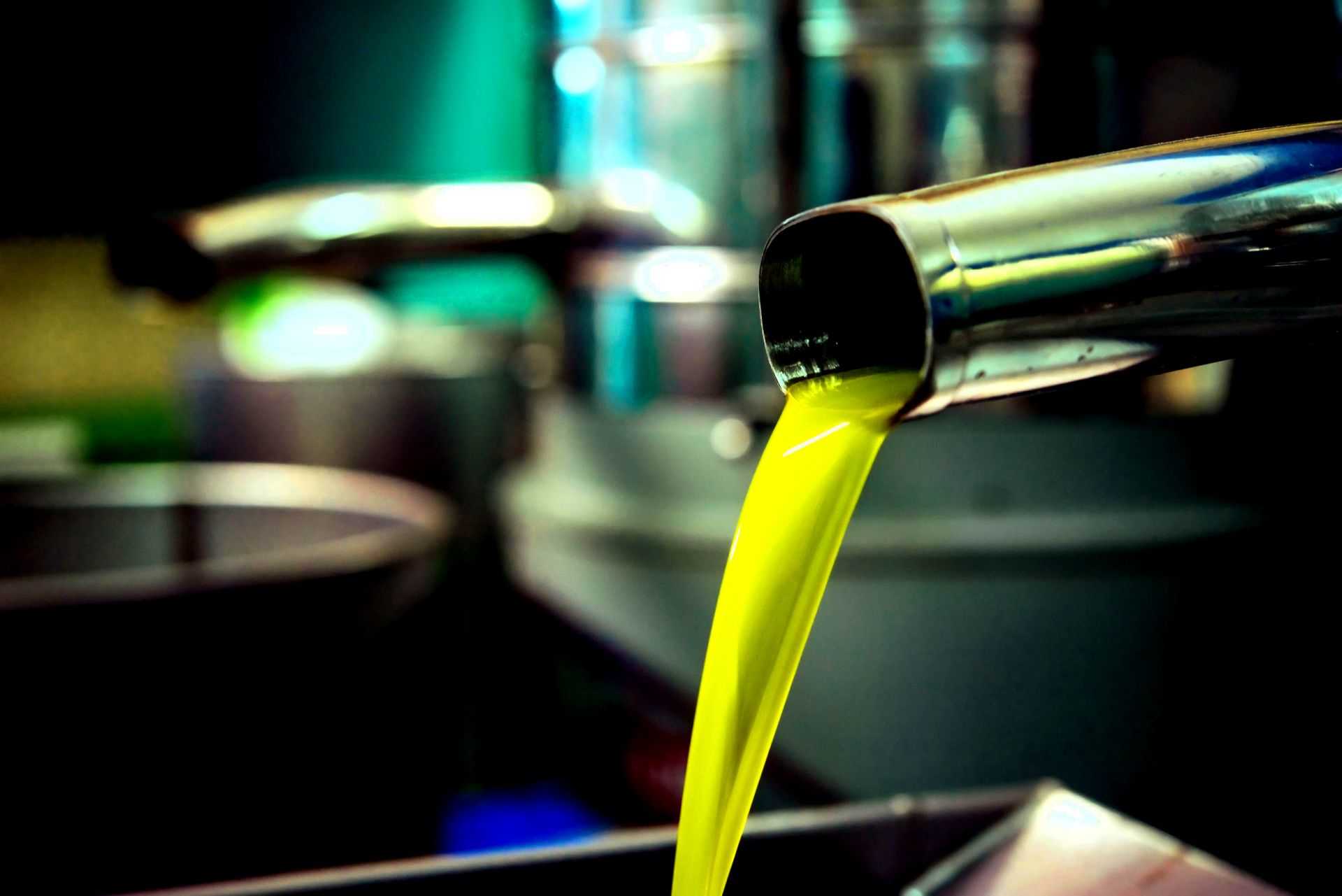 Stream of bright green olive oil pouring from a metal tap into a container. - Olive Oil Times