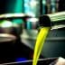 Stream of bright green olive oil pouring from a metal tap into a container. - Olive Oil Times