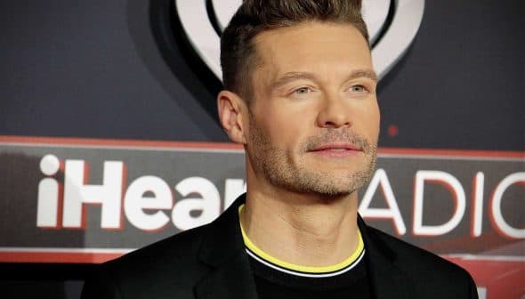 Man wearing a black suit with a yellow collar at an iHeartRadio event red carpet. - Olive Oil Times