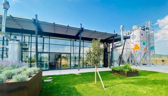 Exterior view of a modern olive oil production facility with glass walls and metal structures. - Olive Oil Times