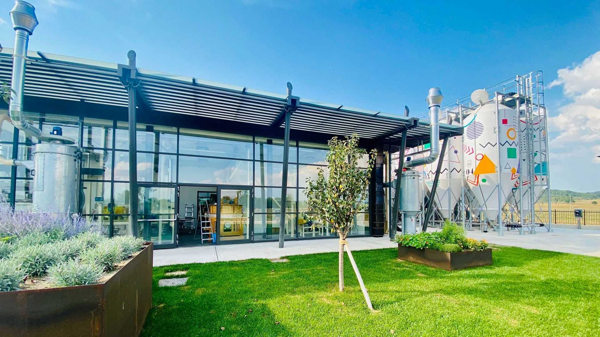 Exterior view of a modern olive oil production facility with glass walls and metal structures. - Olive Oil Times