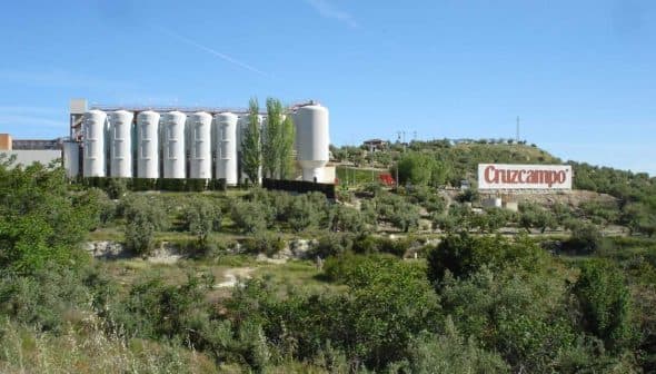 Cruzcampo brewery facility with silos and a large sign in a rural landscape. - Olive Oil Times