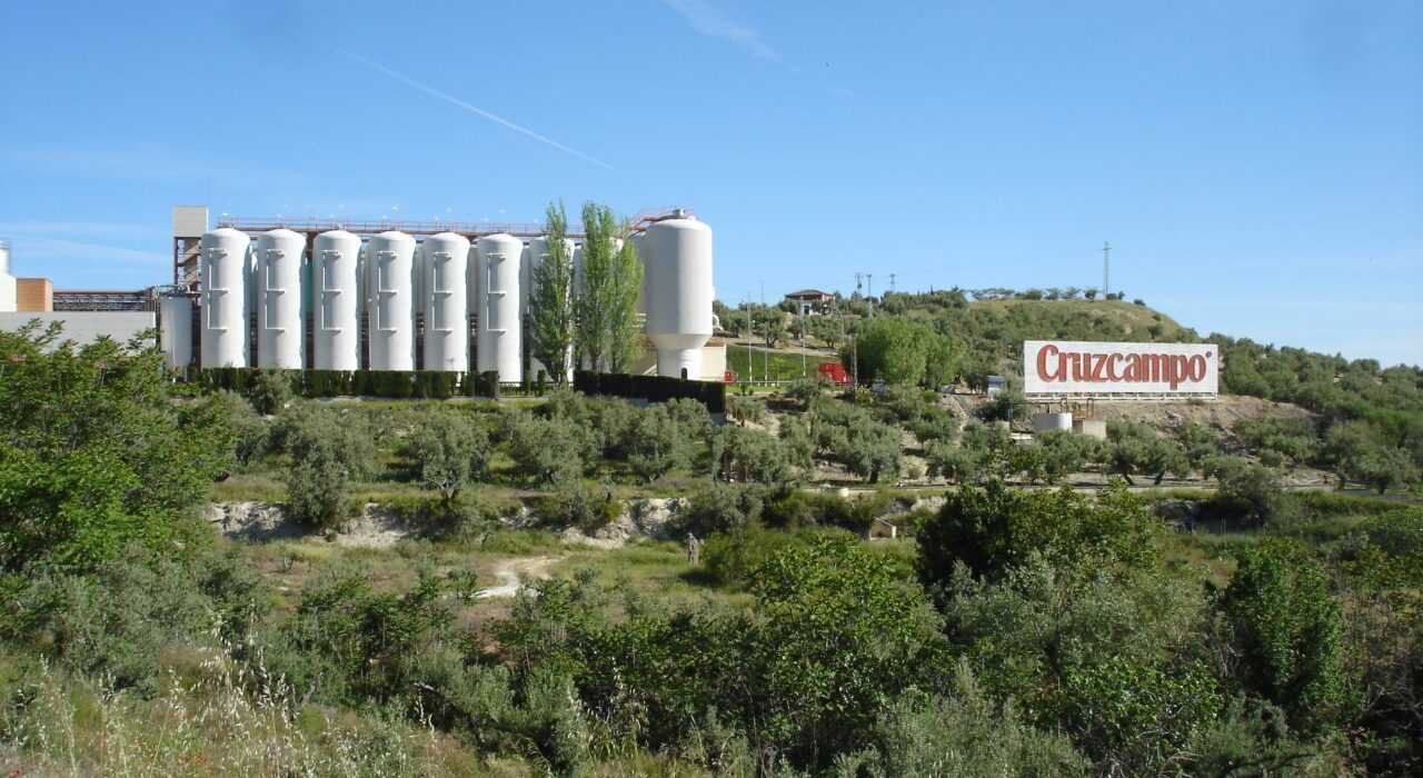 Cruzcampo brewery facility with silos and a large sign in a rural landscape. - Olive Oil Times