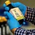 Person wearing blue gloves holding a bottle of California extra virgin olive oil with a label. - Olive Oil Times