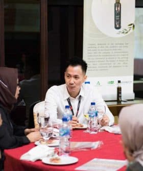 A man in a white shirt engaging in conversation with two women at a round table during a meeting. - Olive Oil Times