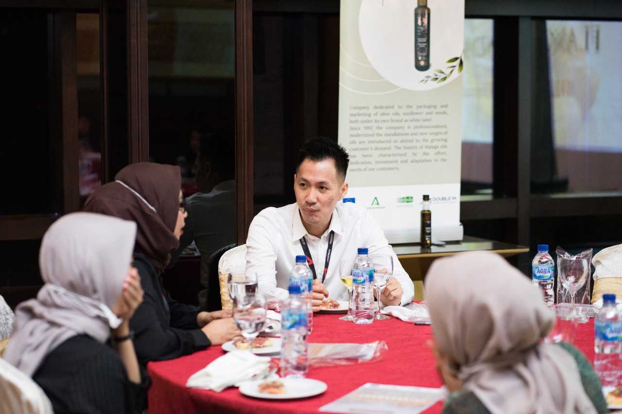 A man in a white shirt engaging in conversation with two women at a round table during a meeting. - Olive Oil Times