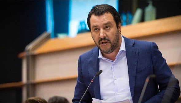 A man in a blue suit speaking at a podium with a microphone in a formal setting. - Olive Oil Times