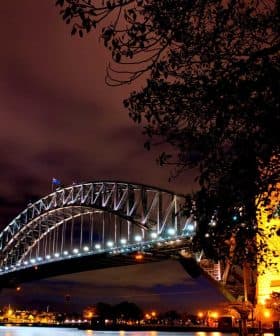 Sydney Harbour Bridge illuminated at night with a clear sky and clouds in the background. - Olive Oil Times